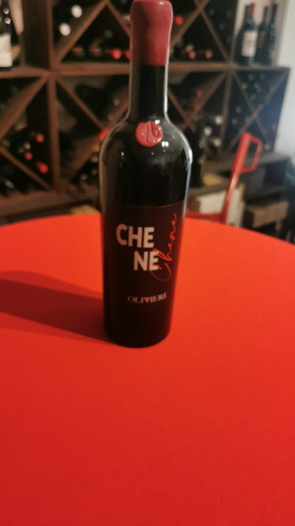 Flasche Chene Rosso auf rotem Untergrund, im Hintergrund ein Weinregal